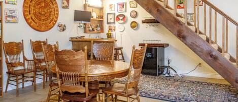 A dining area with a round wooden table and chairs, a staircase, and various wall decorations.