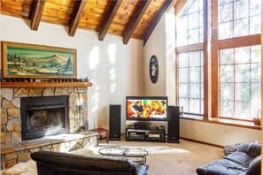 Un salón con chimenea de piedra, televisor y un ventanal con persianas.