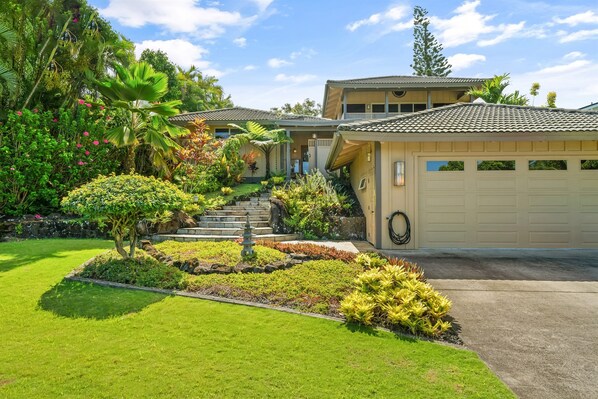 A residential property with a well-maintained garden, a stone staircase leading to the garage, and a two-story house with a tiled roof. - Tropical Zen Oasis -Waterfall Plunge Pool - AC (Princeville)