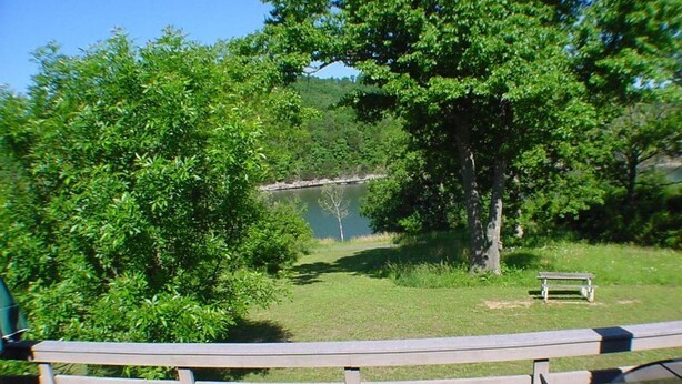 Vista de una zona junto al lago con una cerca de madera, un banco y una mesa de picnic.