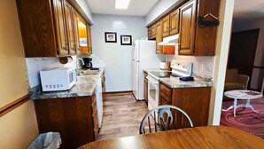 Una cocina compacta con armarios de madera, un refrigerador blanco, un microondas y una estufa. Hay un pequeño comedor con una silla.