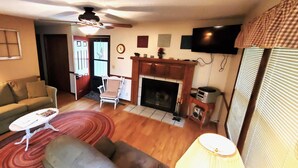 Una sala de estar con sofá, una mesa de centro, chimenea, televisor y ventilador de techo.
