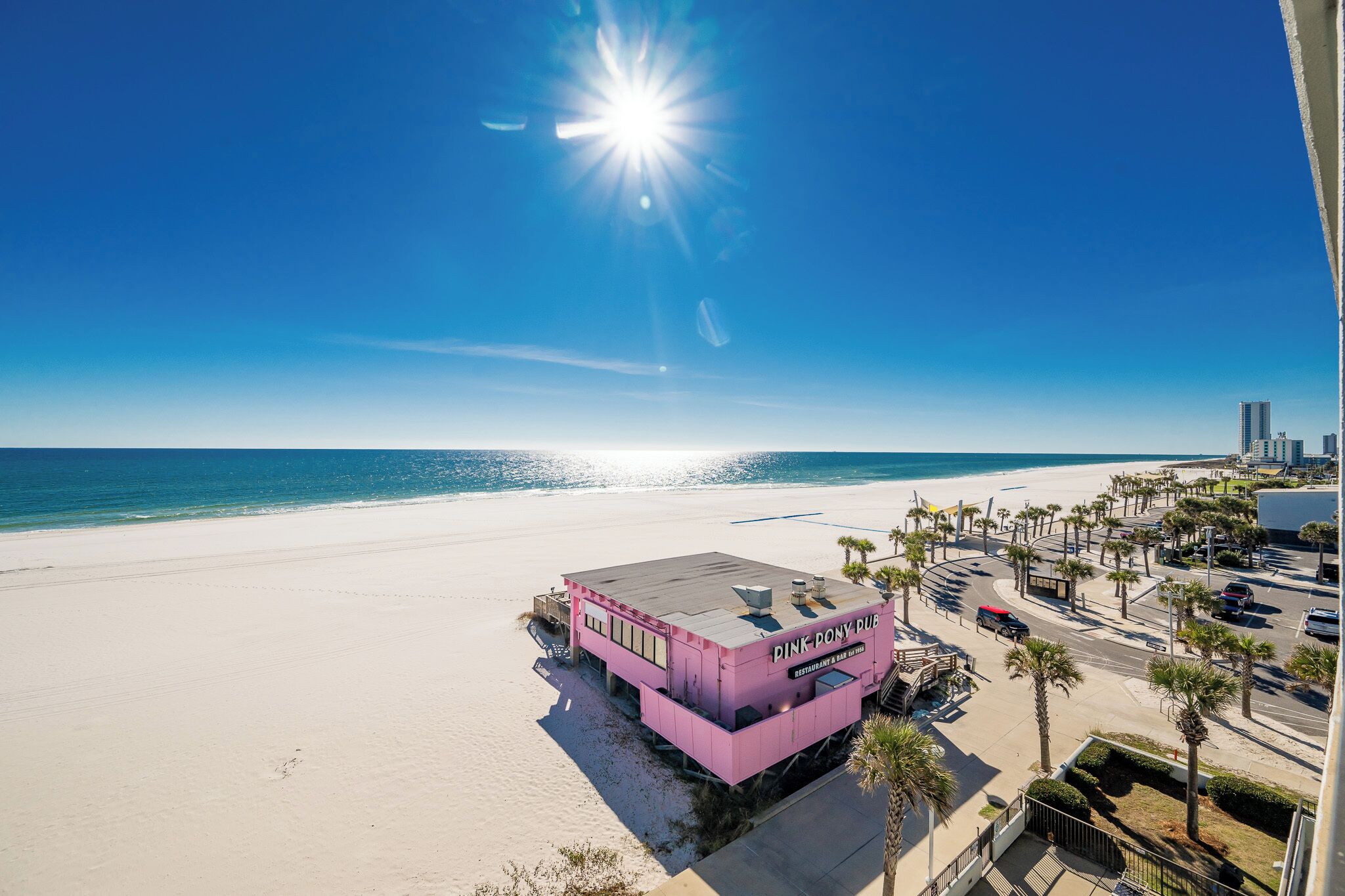 A pink building named 'Pink Pony Pub' on a beach with a clear sky and ocean view.