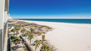 A beach view from a balcony with a clear sky, a sandy beach, and a few palm trees.