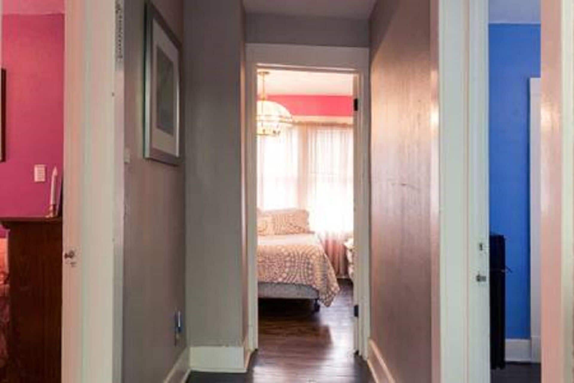 A narrow hallway leading to a bedroom with a bed and a window.