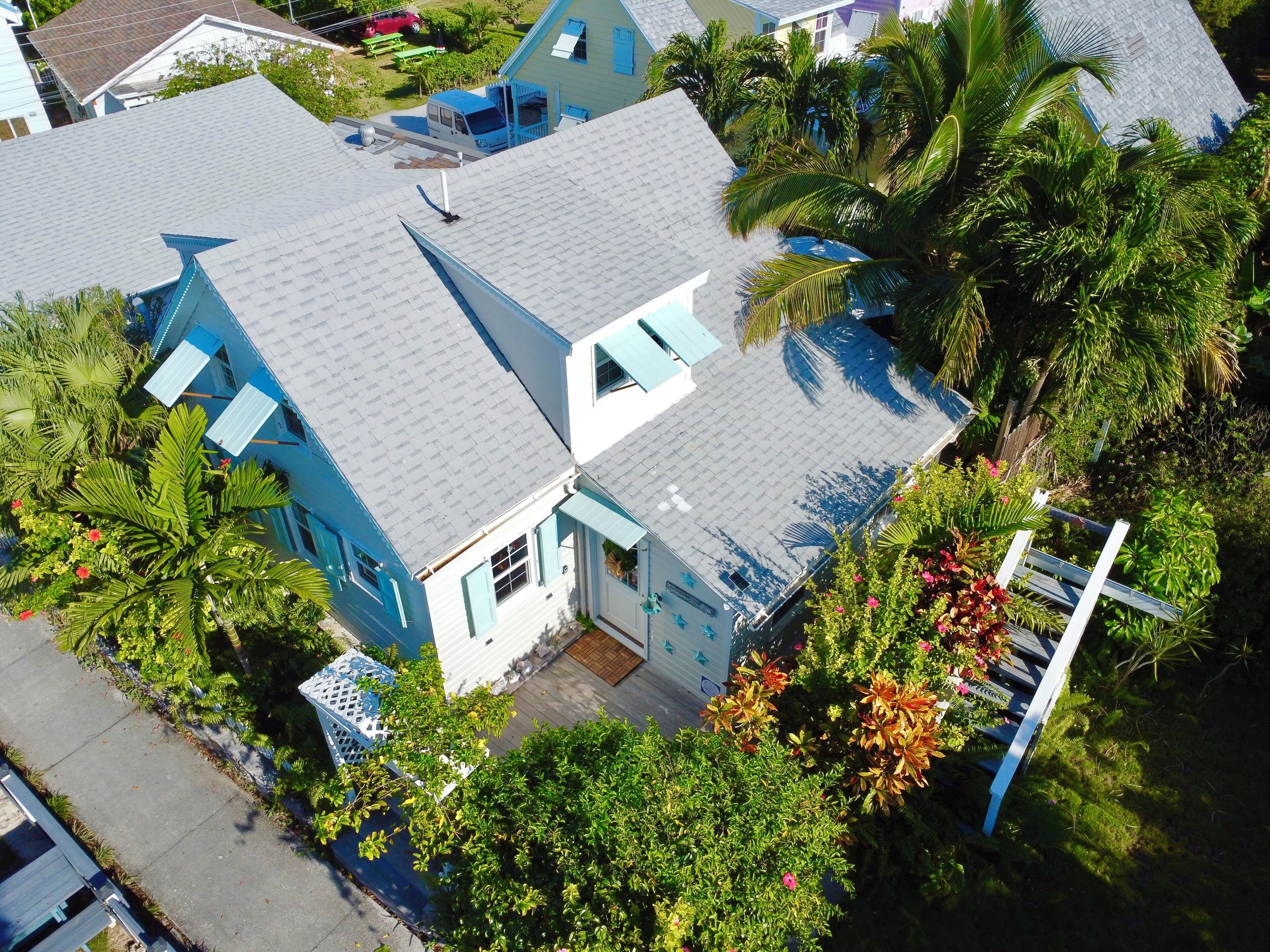 A large house with a grey roof, surrounded by lush greenery and palm trees.