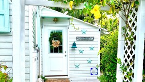 A white wooden porch with steps leading to a door, decorated with star-shaped ornaments and a bell. - Dunwanderin-Historic Cottage in the Heart of Hope Town w/dock (Elbow Cay)