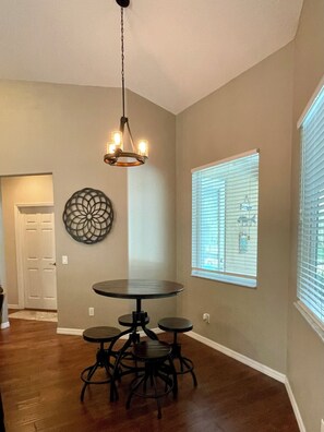A dining area with a round table and four chairs, a chandelier, a decorative wall piece, and a window with blinds. - Spacious, fully furnished family friendly 3 bedroom home with private pool. (Lecanto)