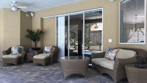Une terrasse ensoleillée, meublée de meubles en osier, dotée d’un ventilateur de plafond et offrant une vue sur une piscine.