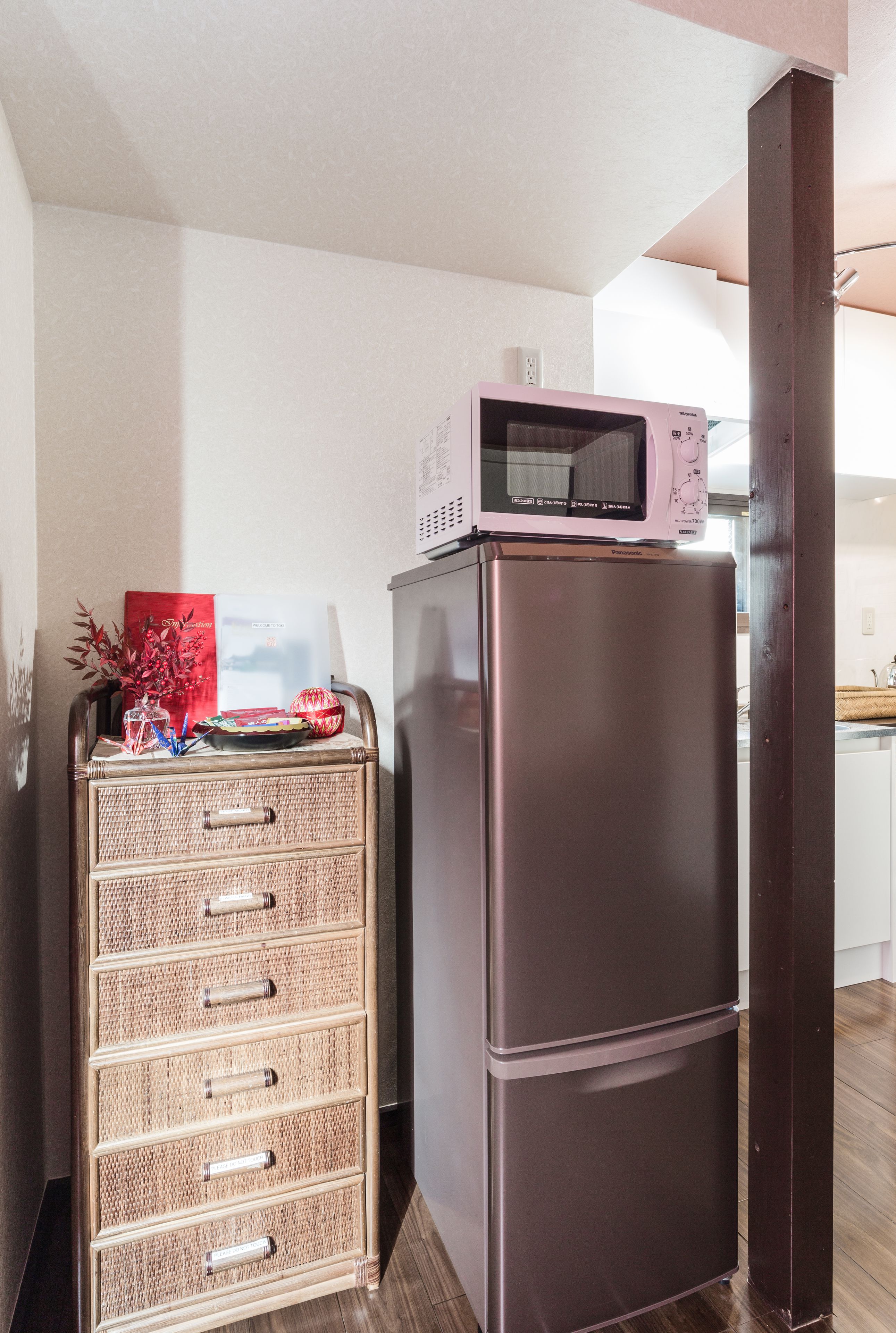 A kitchenette with a stainless steel refrigerator, a microwave, and a wicker storage unit.