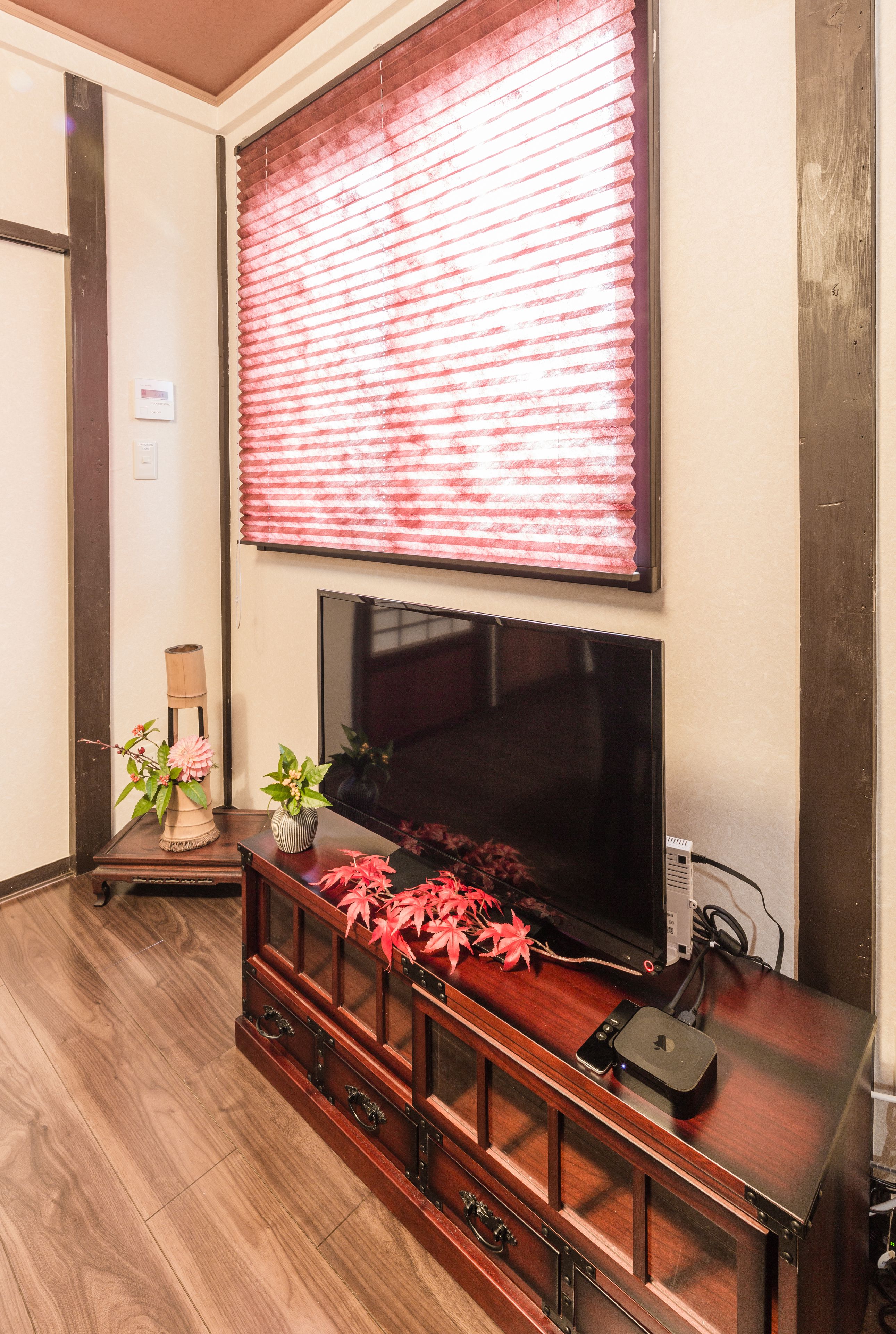 A living room with a large flat-screen TV mounted on the wall, a wooden entertainment center with drawers, and a potted plant on the side table.
