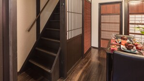 Una escalera de madera con barandilla de metal, un comedor con mesa dispuesta para dos comensales y una puerta corrediza tradicional.