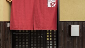 Una entrada de edificio con un paño rojo, una puerta de madera con diseño de rejilla y un tejado de tejas.