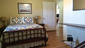 Une chambre à coucher comprenant un lit, une table de chevet, une lampe, un tableau encadré accroché au mur et une porte donnant sur une autre pièce.