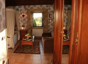 A cozy room with a bed, a wooden cabinet, a small table with a plant, a window with a view of the outdoors, and a stone wall. - Casa Do Sear (Sanxenxo)