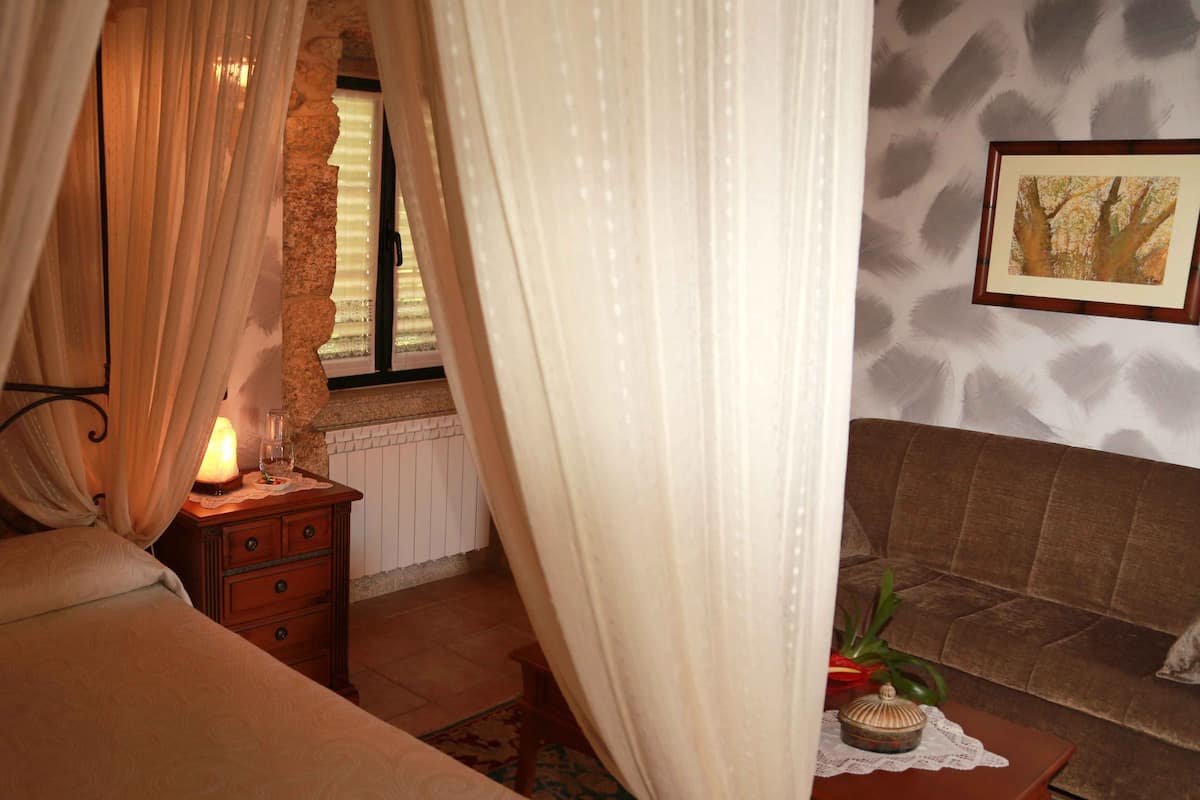 A bedroom with a bed, a nightstand with a lamp, a dresser, and a sofa.