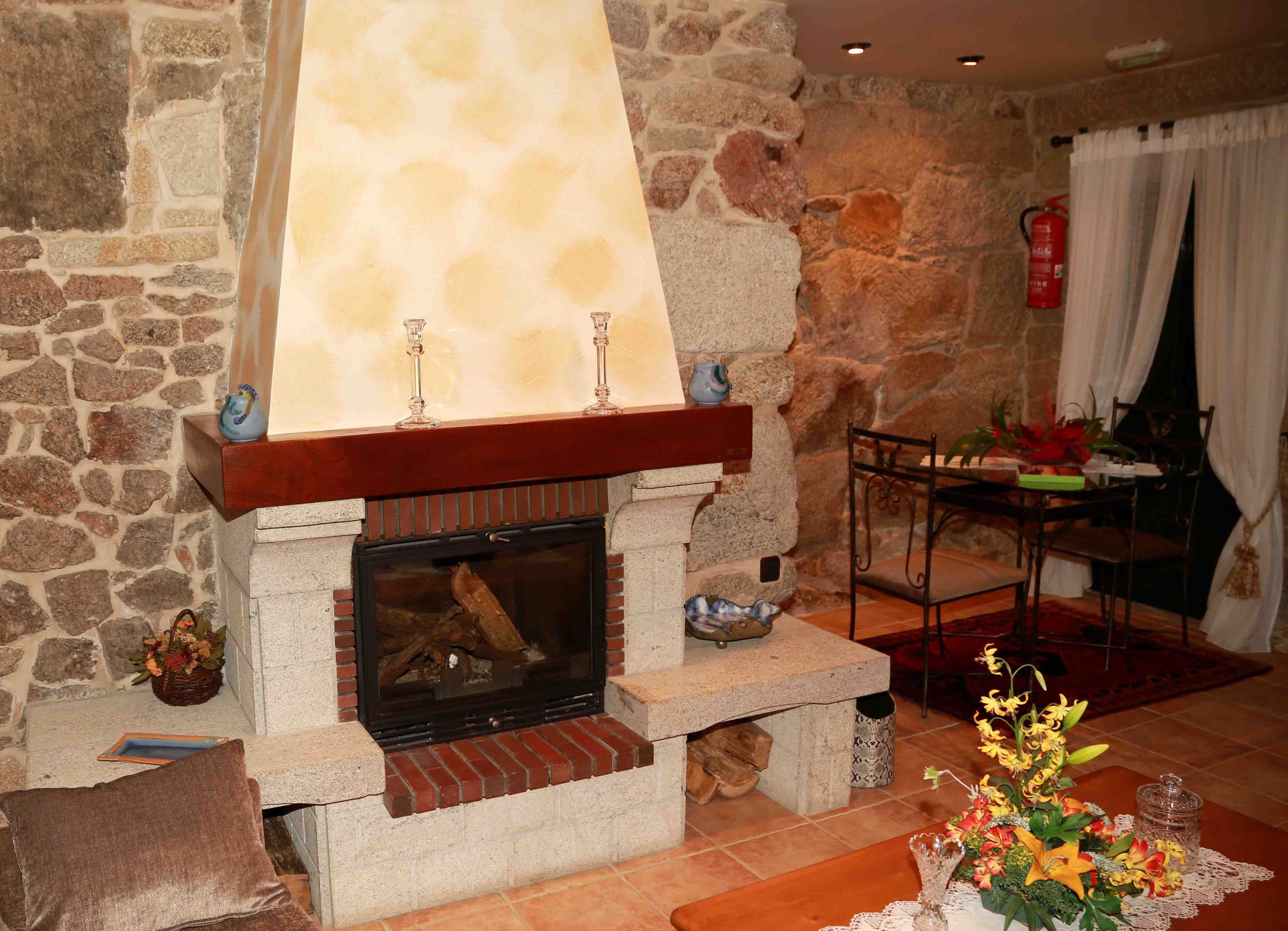 Una chimenea de piedra con repisa, una mesa con sillas y un florero con flores.