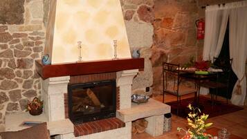 Una chimenea de piedra con repisa, una mesa con sillas y un florero con flores.