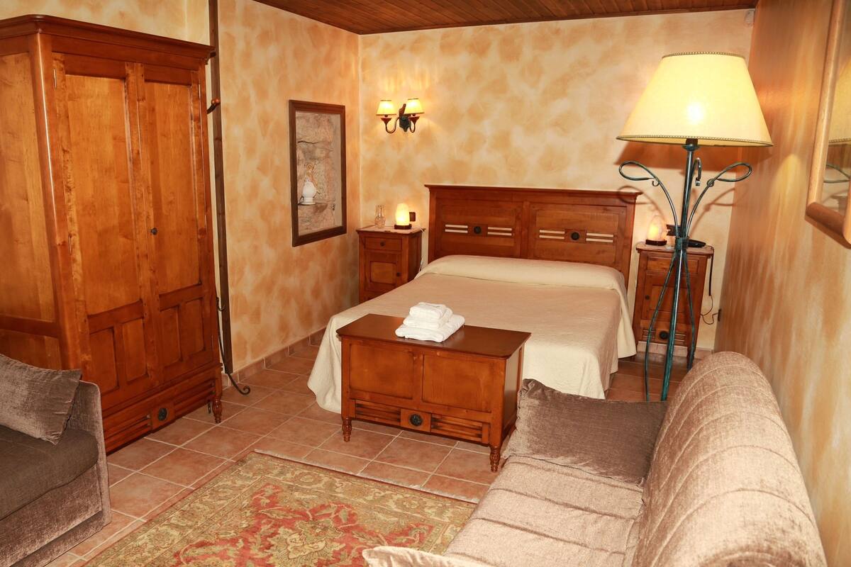 A cozy room with a bed, a wooden wardrobe, a sofa, a nightstand, and a lamp.
