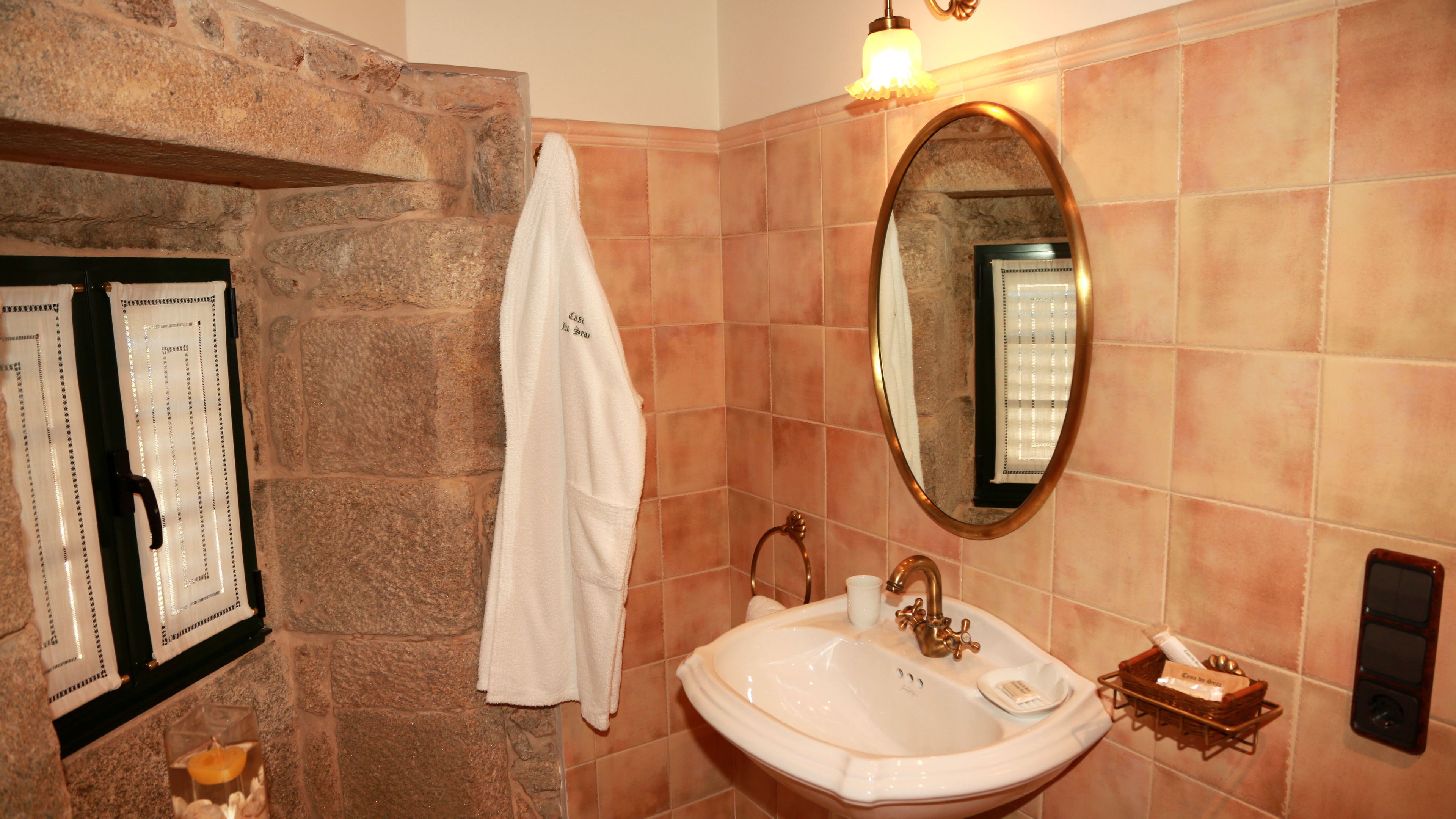 Un baño con pared de piedra, un lavamanos blanco con grifo dorado, un espejo y una toalla colgada en la pared.