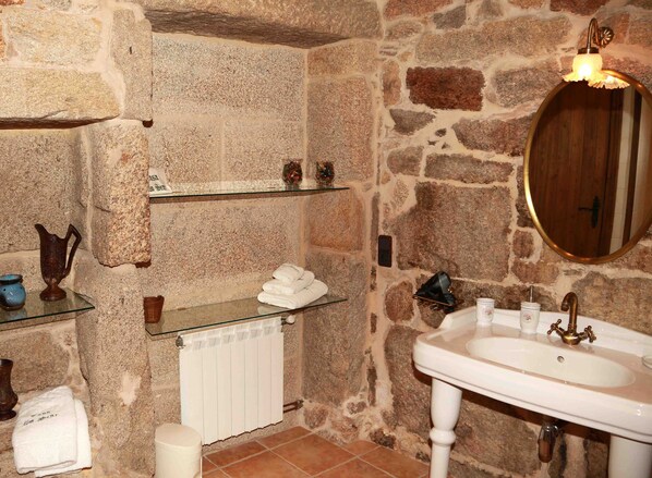 Une salle de bain aux murs en pierre, avec un lavabo blanc, un miroir et un radiateur.