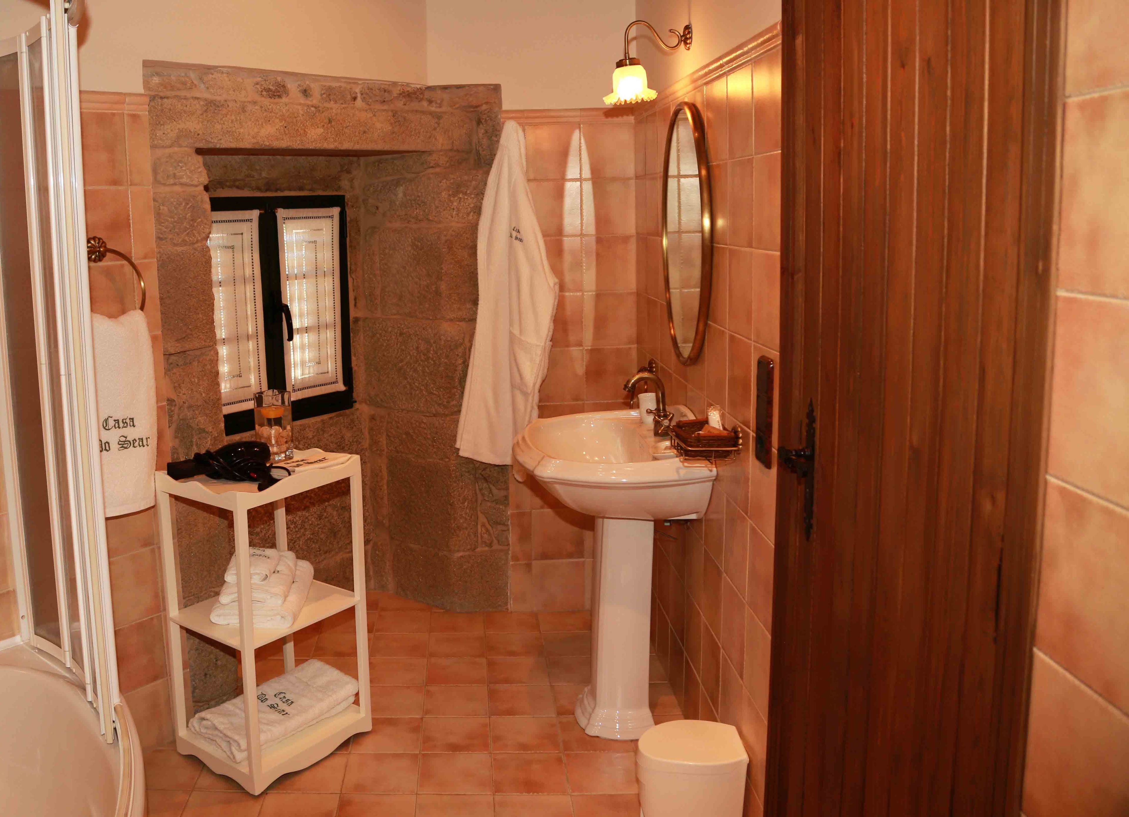 A bathroom with a stone wall, a white sink, a mirror, a towel rack, and a shelf with towels.