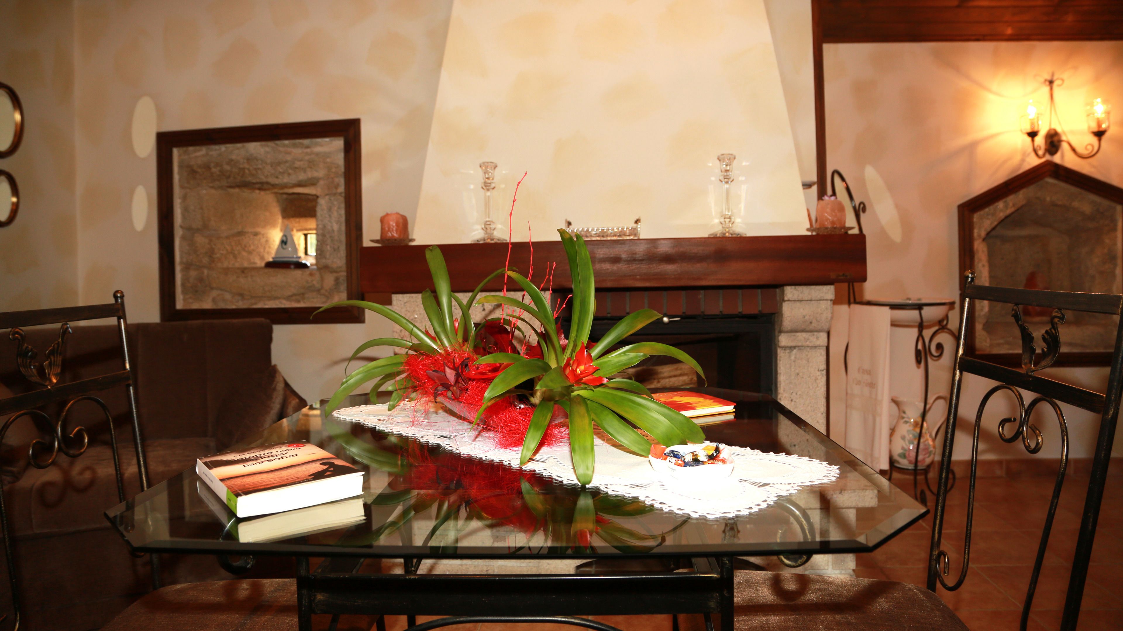 A dining table with a glass top, surrounded by chairs, in a room with a fireplace and framed artwork on the wall.