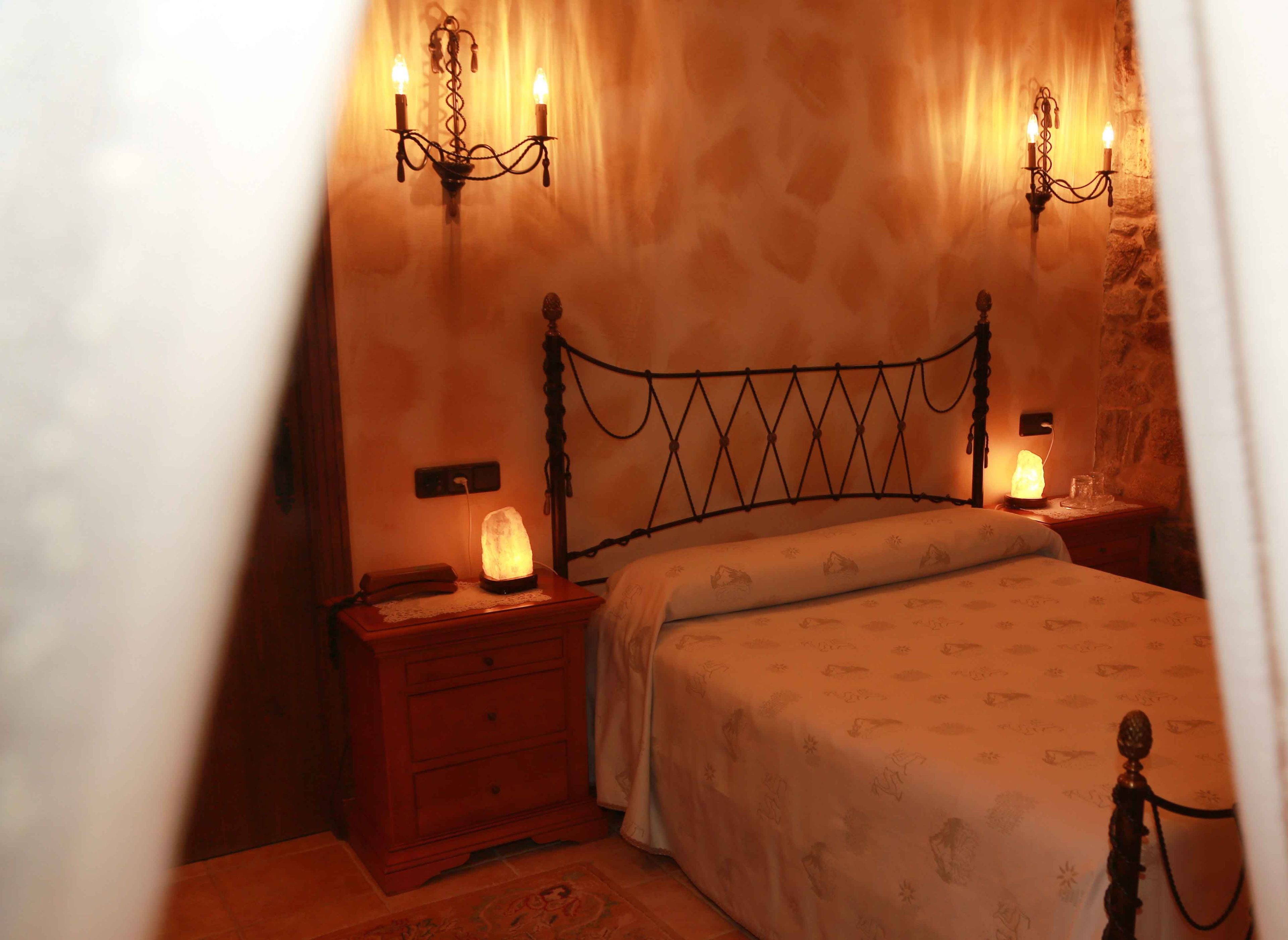 A bedroom with a wooden bed, a nightstand with a salt lamp, and a wall-mounted candelabra.