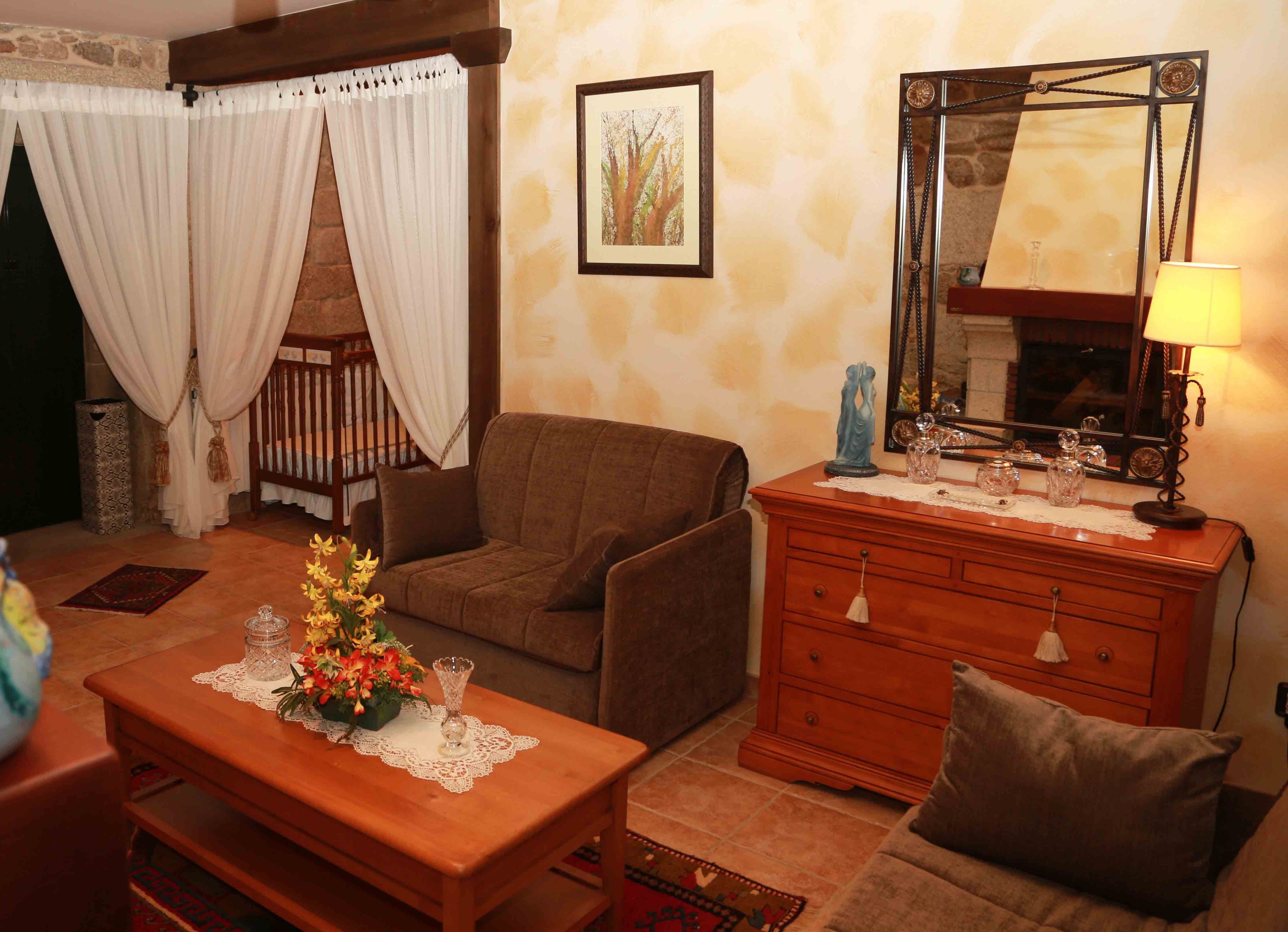 Un salon chaleureux avec un canapé marron, une table basse en bois agrémentée d’un centre de table floral, une commode en bois avec un miroir et une lampe.