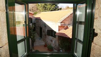 A view through a window of a stone building with a tiled roof, a small staircase, and potted plants.