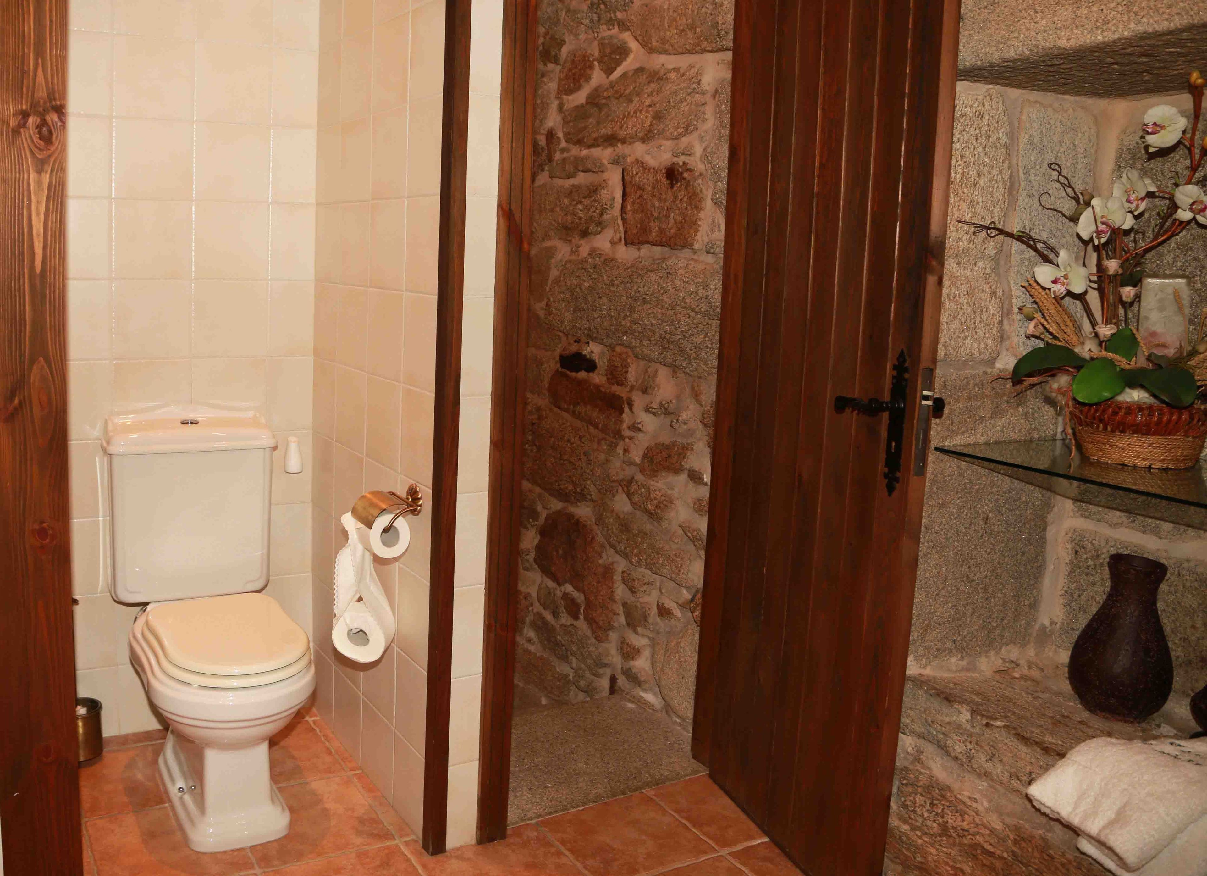 Un baño con inodoro, rollo de papel higiénico, pared de piedra y puerta de madera.