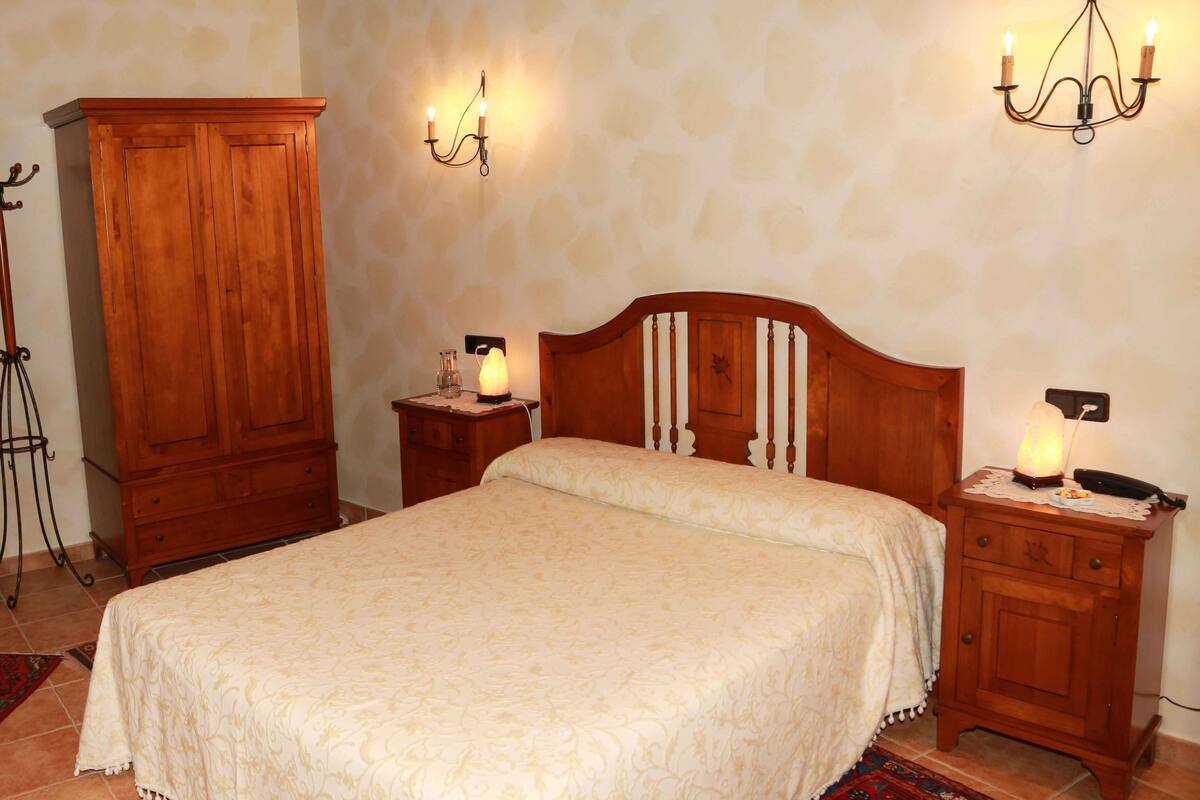 A bedroom with a wooden bed, nightstands with lamps, a wooden wardrobe, and a wall-mounted light fixture.