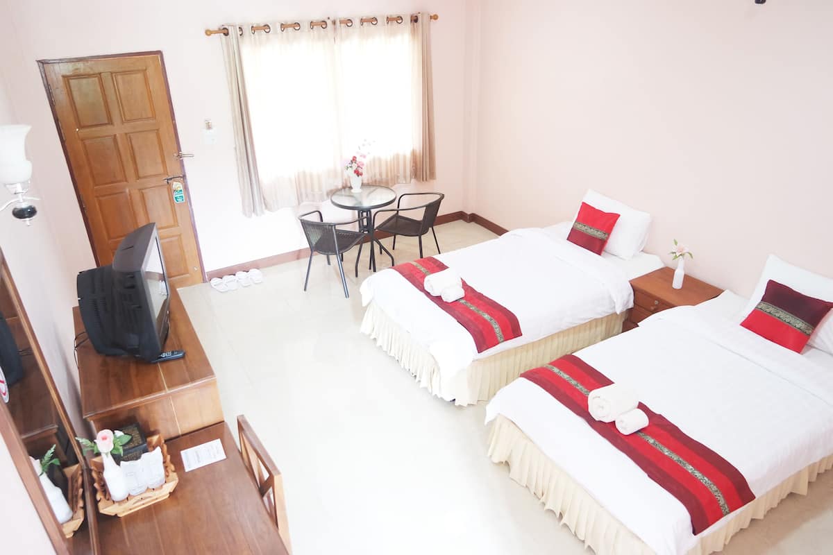 A hotel room with two beds, a desk with a computer, a small table with chairs, and a window with curtains.