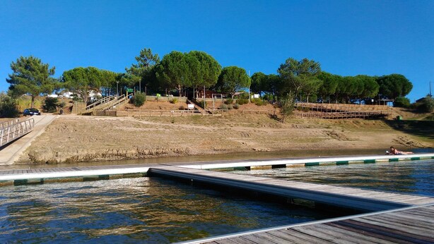 Una piscina con plataforma de madera, rodeada de árboles y una ladera con una escalera de madera.