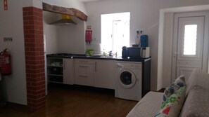 A compact kitchen with a washing machine, a microwave, and a stove. There is a fire extinguisher mounted on the wall.