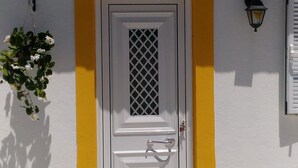 Una puerta blanca con una rejilla metálica, una pared amarilla y un techo de tejas rojas.