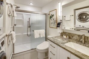 A modern bathroom with a glass-enclosed shower, a toilet, a sink with a granite countertop, and a built-in washing machine. - Ute Condominiums - Central & Cozy (Aspen)