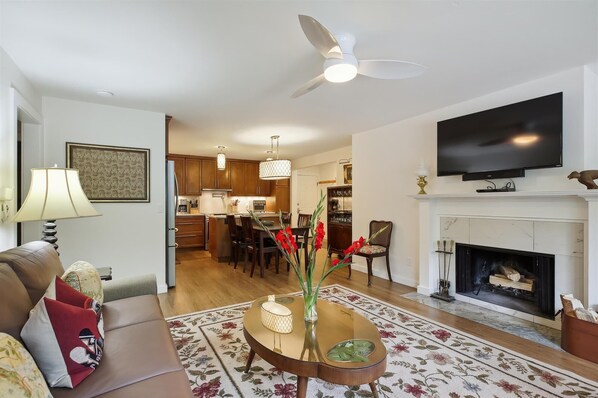 A living room with a sofa, coffee table, fireplace, TV, and kitchen in the background. - Ute Condominiums - Central & Cozy (Aspen)