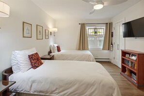 A hotel room with two beds, a flat-screen TV, a bookshelf, and a window with curtains. - Ute Condominiums - Central & Cozy (Aspen)