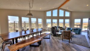 A spacious room with a large wooden dining table, multiple chairs, and a cozy seating area with a sofa and armchairs. Large windows provide a view of the beach. - Oceanfront on Sandy Beach! Hot Tub! Dog Friendly! Direct Beach Access! Game Room! (Waldport)