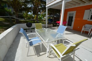 An outdoor patio with a glass-top table and white chairs with blue and yellow cushions.