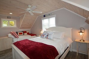 A bedroom with a sloped ceiling, two beds, a ceiling fan, a window, and a bedside lamp.