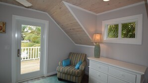 Una habitación con techo de madera, un tocador blanco, un sillón estampado y una ventana con vistas a la vegetación.