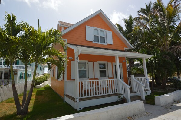 A single-story house with a porch, surrounded by palm trees and a white picket fence.