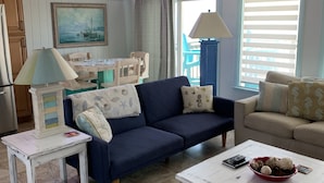 Uma sala de estar aconchegante com um sofá azul, uma mesa de centro branca e um espaço de jantar com mesa e cadeiras de madeira.