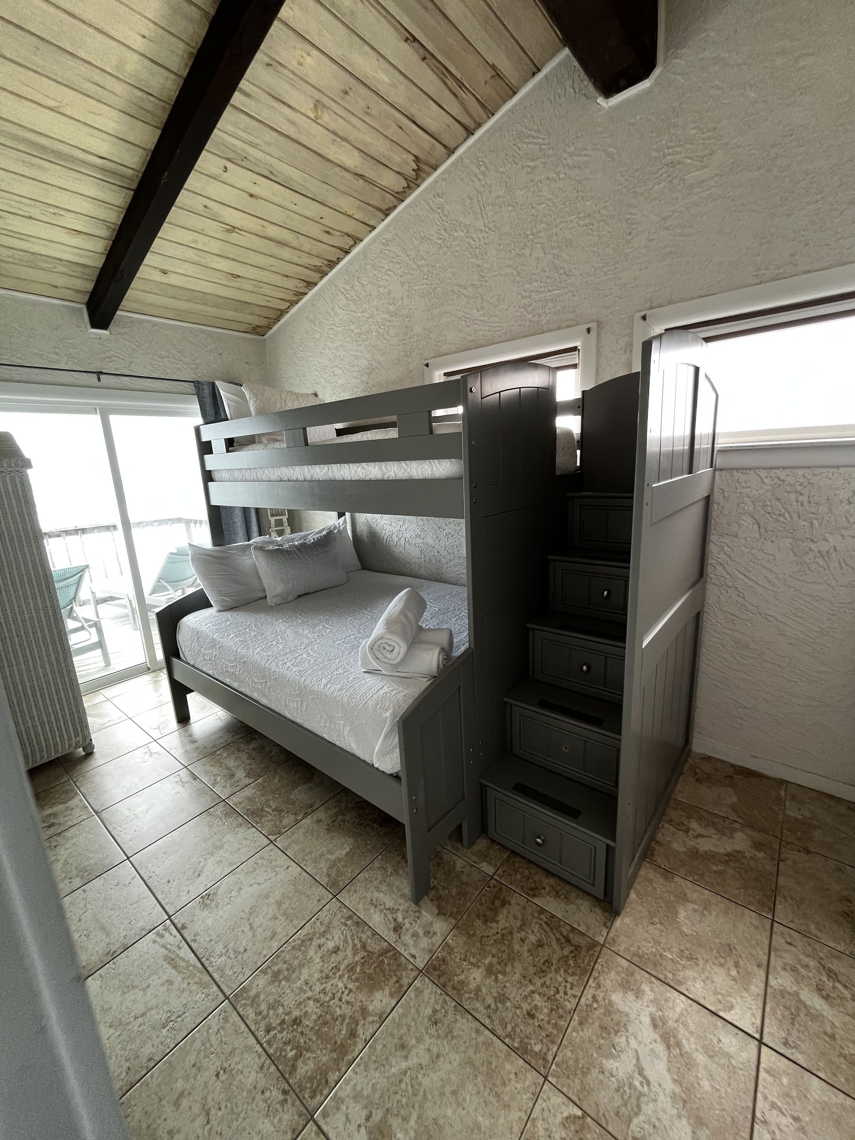 A bunk bed with a pull-out desk, a small wardrobe, and a window.