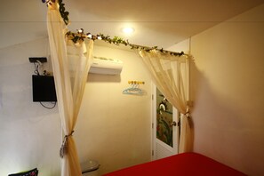 A room with a bed, a wall-mounted air conditioner, a small shelf, and a door with a colorful mural. - Miyabi Resort (Koh Lan)