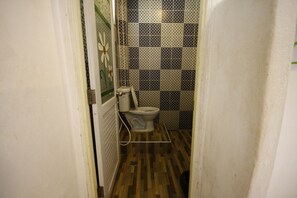 A small bathroom with a toilet, a shower, and a wooden floor. - Miyabi Resort (Koh Lan)