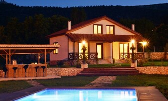 Una casa de dos pisos con piscina, escalones de piedra e iluminación exterior.