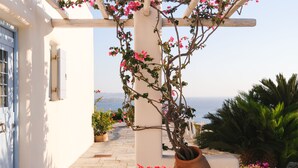 A white building with a stone pathway leading to a white pergola with pink flowers. - Spacious Luxury Villa Delion-stunning sunset&bay view, infinity pool, by beaches (PAROS)